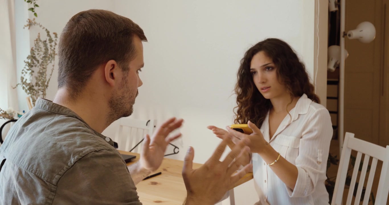 Žena bere muži smartphone, aby zkontrolovala jeho zprávy během vyhrocené partnerské hádky.