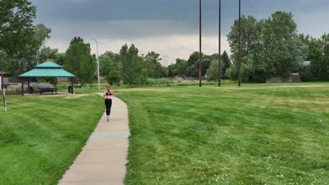 a woman runs along a city park pathway. athletic and slim she inspires others to get outdoors and stay fit. slow motion drone 4k