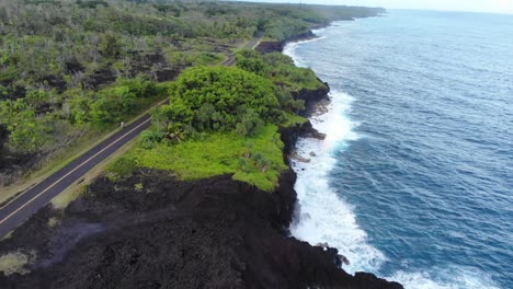 black volcanic rock cliffs and a road that passes along it through jungle on hawaii island