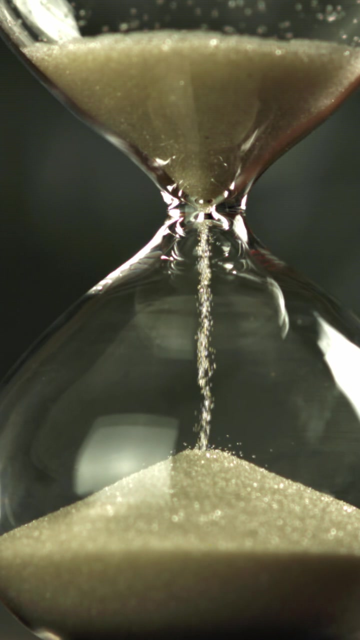 Sand Flowing Through a Glass Hourglass on a Dark Background