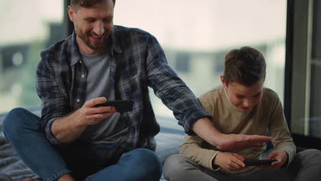 Father-and-son-gaming-mobile-phones.-Dad-and-boy-spying-each-other-smartphones.