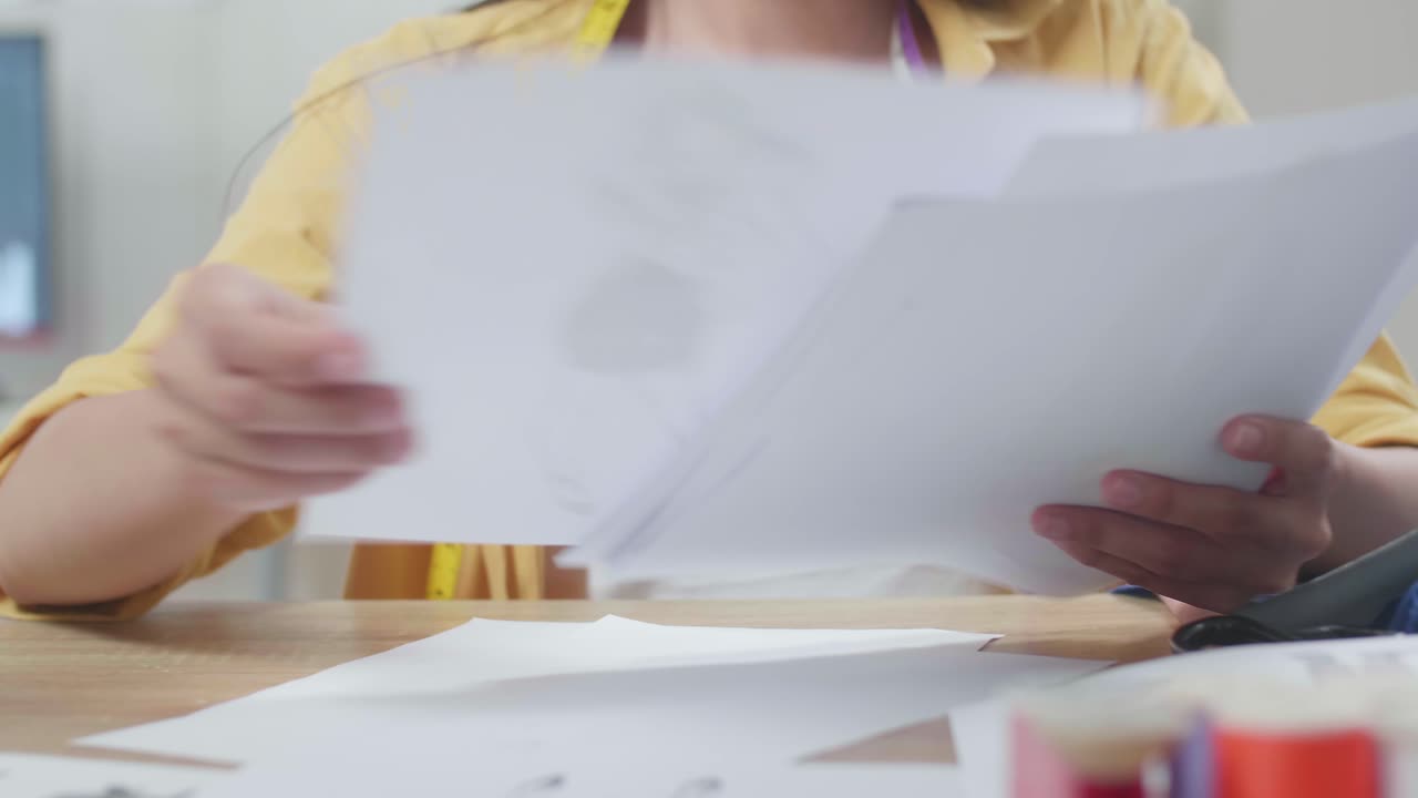 primer plano de una mujer diseñadora asiática sonriente reorganizando los papeles mientras diseña ropa en el estudio