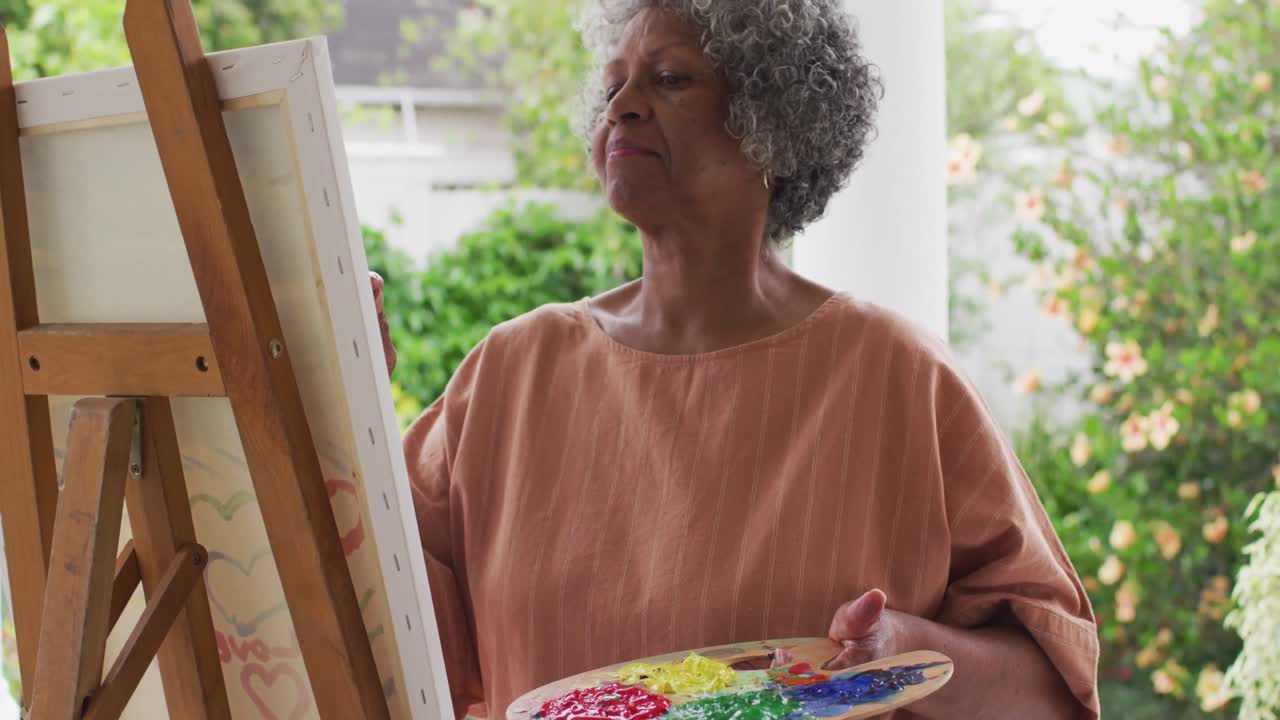 mulher afro-americana sênior pintando enquanto está de pé na varanda da casa