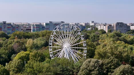 rotating aerial view of a white ferris wheel surrounded by oraselul copiilor park in bucharest, romania