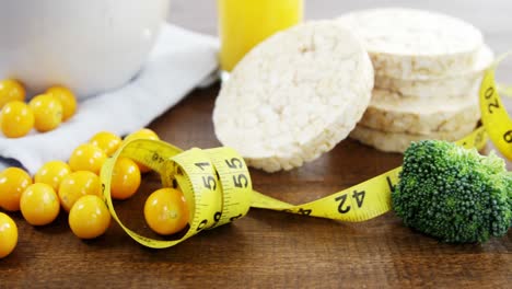 Broccoli,-granola-bar,-yellow-cherries-and-measurement-tape-on-wooden-table