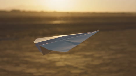 paper airplane soaring against a warm sunset horizon
