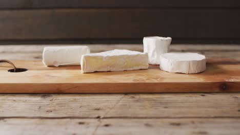 Video-of-assorted-soft-cheeses-on-chopping-board,-on-wooden-table-with-copy-space