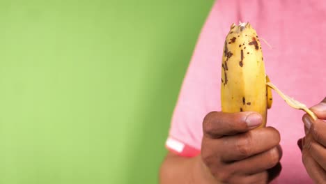 mano sosteniendo un plátano amarillo con la piel descascarada en la pantalla verde,