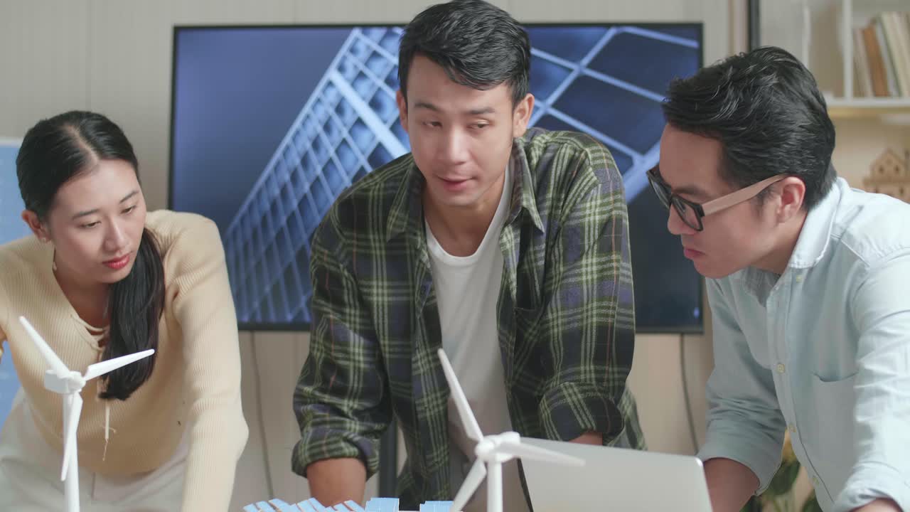 아시아 엔지니어 그룹이 사무실에서 태양 전지판을 가진 작은 집 모델에 대한 회의를 하고 있습니다.