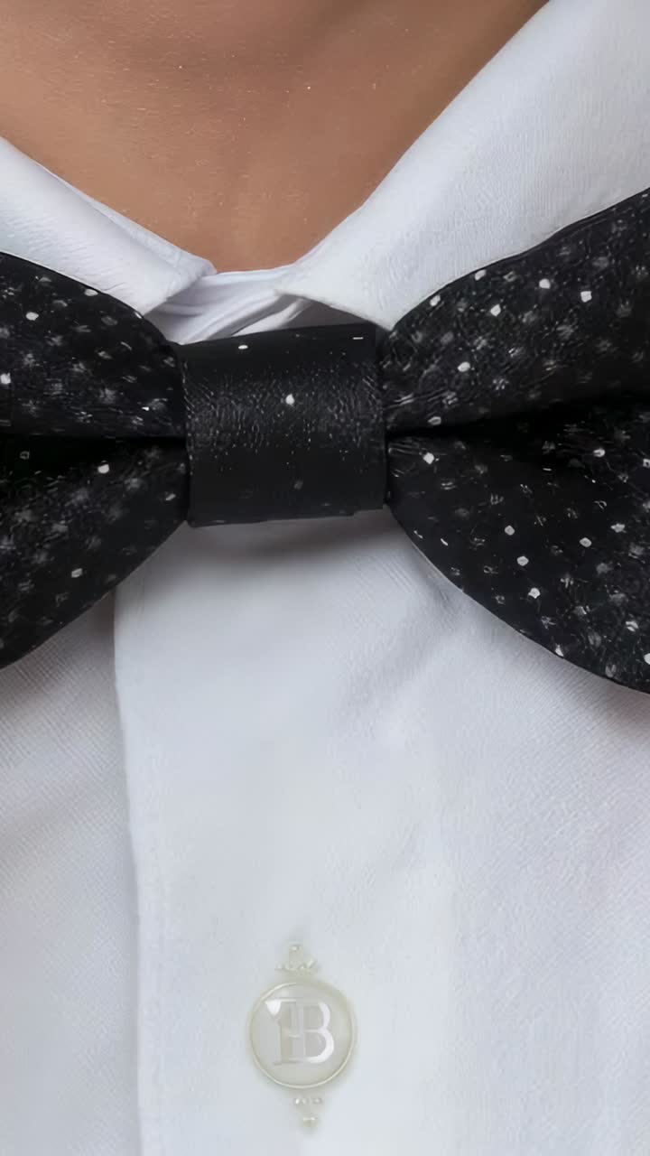 Vídeo vertical: adulto respirando con camisa blanca moviendo pajarita negra de lunares en un set con B stud