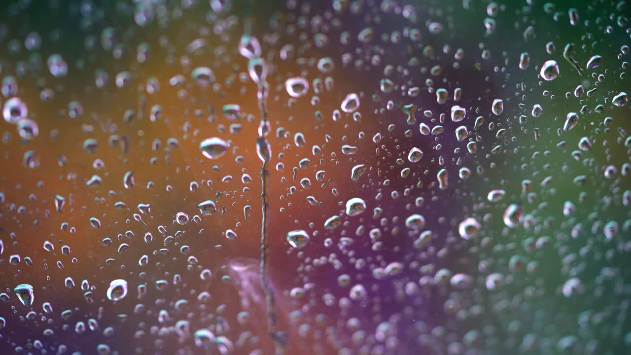 Droplets on colorful background. Raindrops flow down the glass window. Drops of water falls into the window. Close-up.