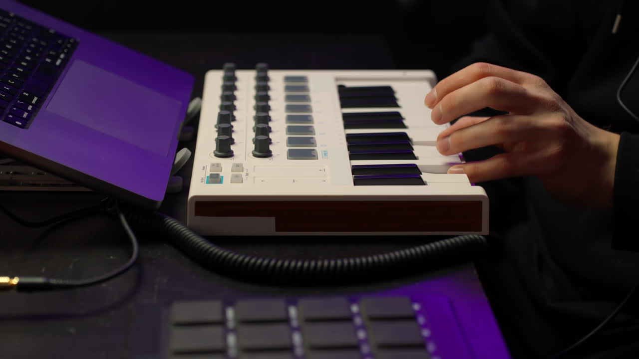 Musician's hand expertly playing MIDI keyboard controller, composing electronic tracks or songs with laptop and digital audio workstation in a home studio environmentm, close up , artificial lightnig