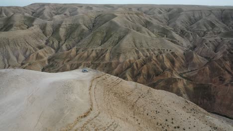 Impresionante-Inclinación-Hacia-Abajo-En-Un-Automóvil-Parado-En-Un-Acantilado,-Desierto-De-Judea,-Israel,-Toma-Aérea