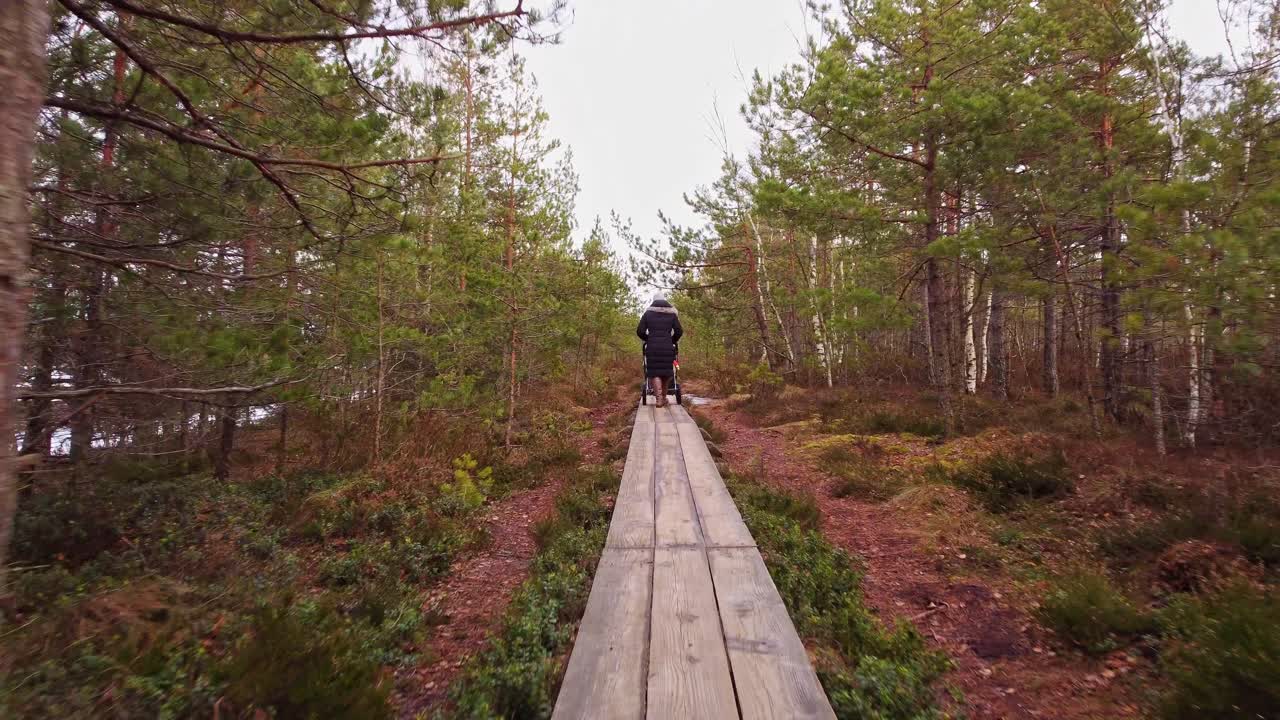 숲속의 좁은 나무 통로에서 유모차와 씨름하는 사람