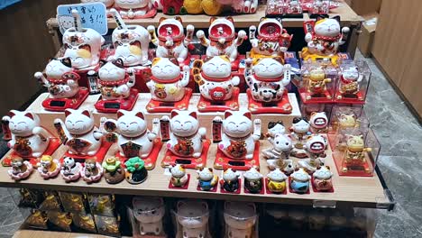 a wide range of waving lucky fortune cats is displayed on a tiered shelf, all with their left paws moving