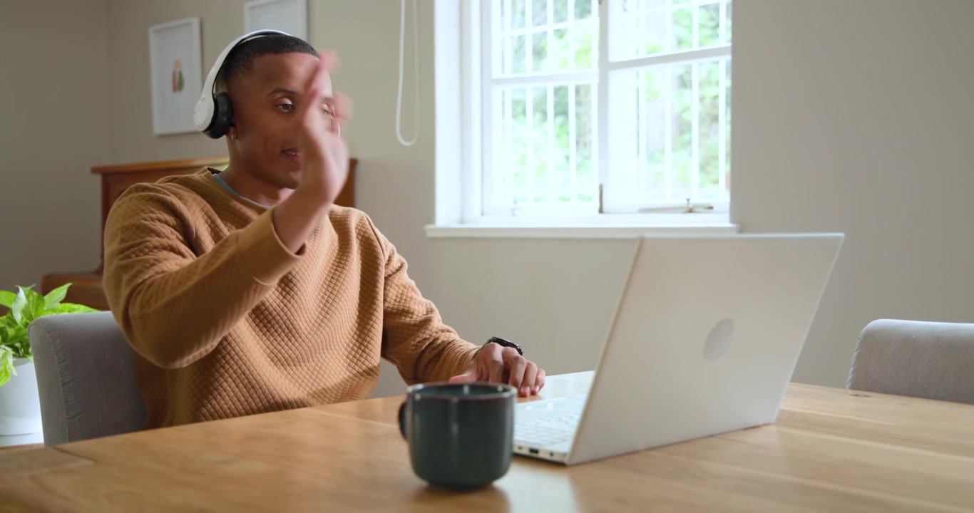 African American man in tan knit typing reaching headphones putting on joining laptop call at home