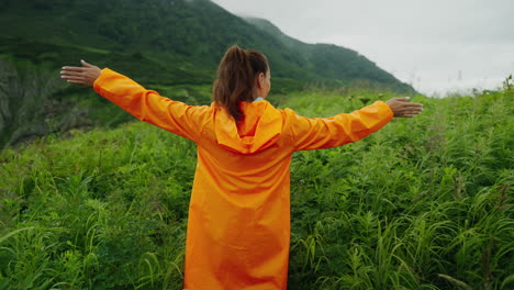 woman in orange raincoat enjoying a mountain view