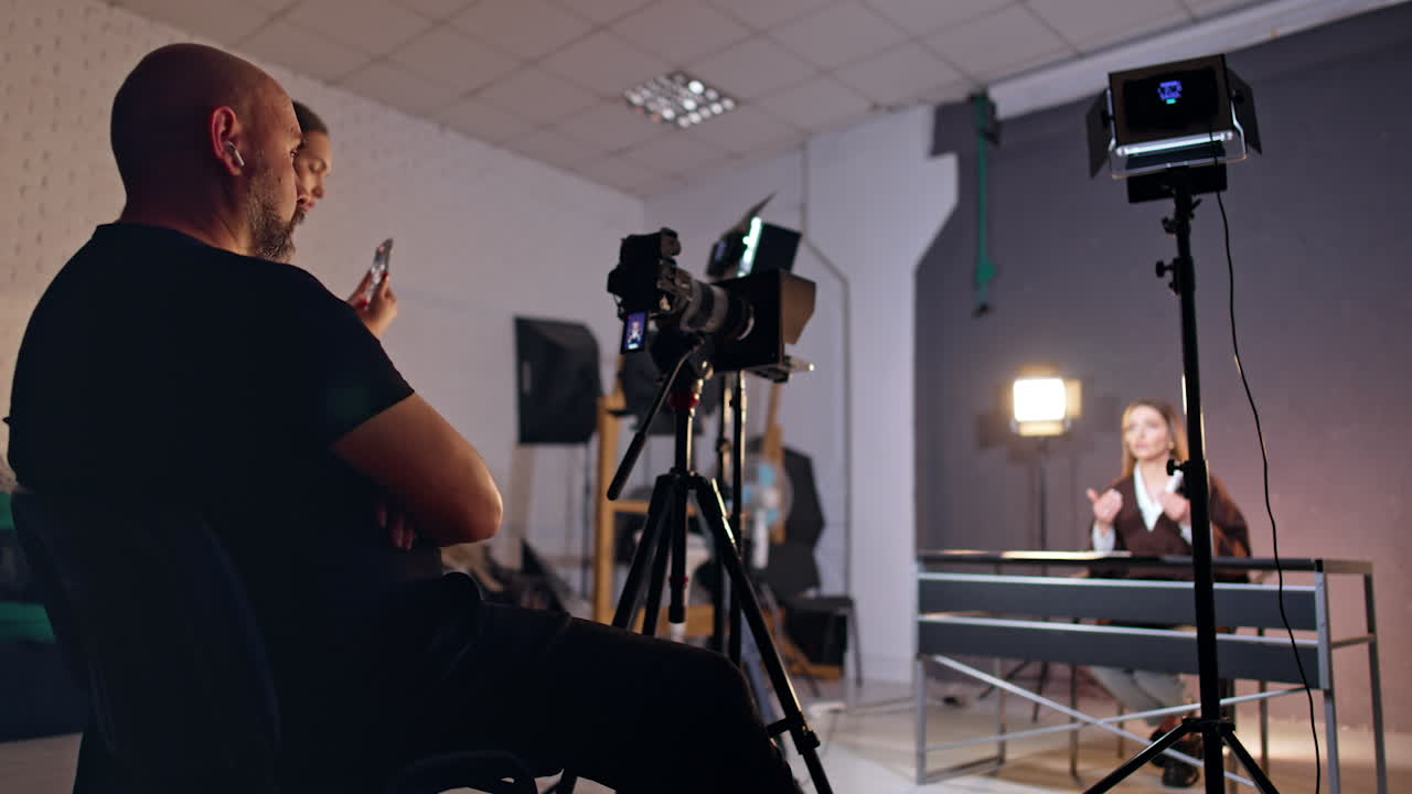 Side view of a male photographer working in photo studio. Cameraman shooting a program with female reporter.