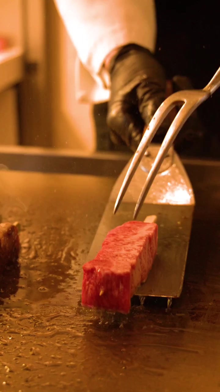 シェフがヘラとフォークを使って霜降り牛肉の串焼きを焼くクローズアップショット。