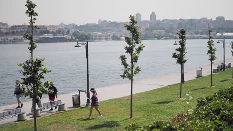 people walking along a waterfront park with a view of the city in the background