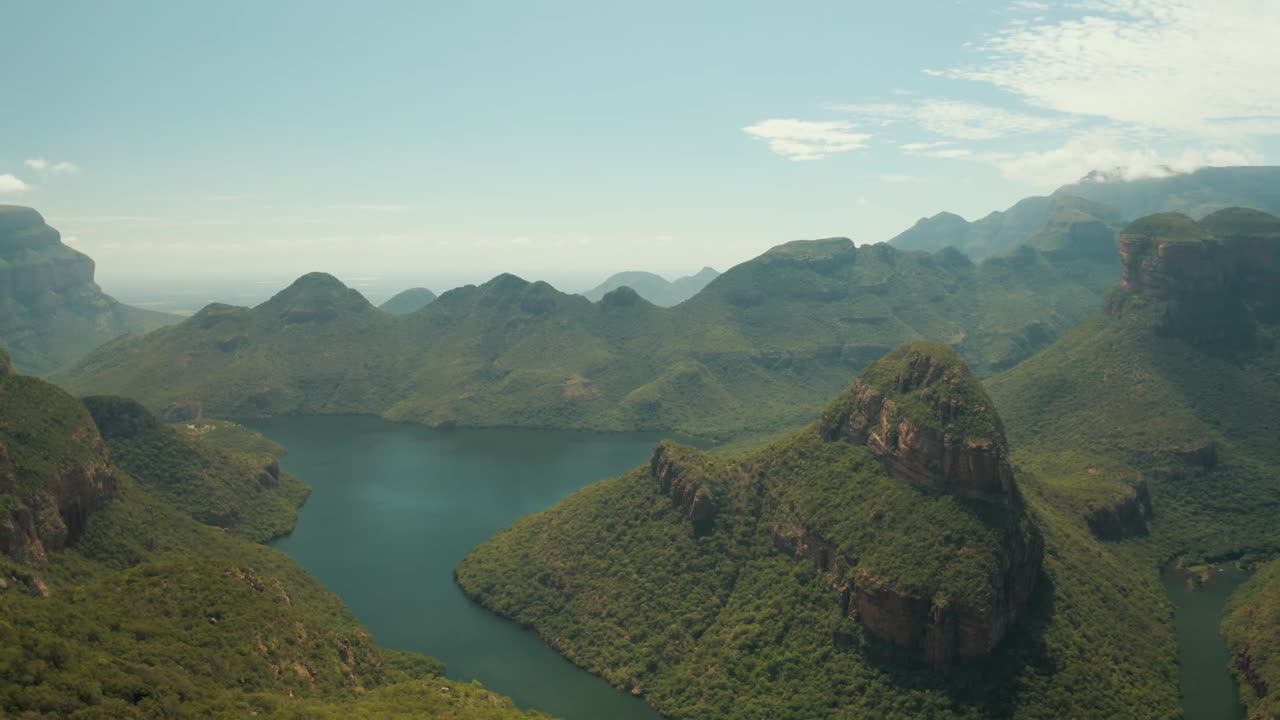 Soar above the magnificent Blyde River Canyon, South Africa, one of the world's largest. This footage captures the winding river, lush green mountains, and dramatic cliffs of this breathtaking wonder.
