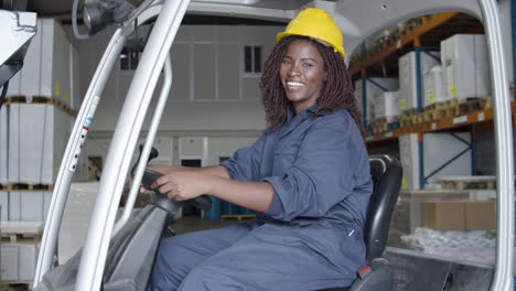 happy african american female worker sitting in forkfit and looking at the camera