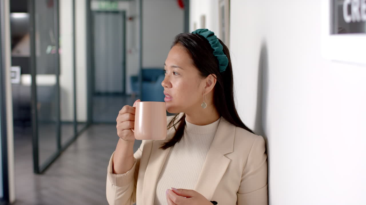 Holding coffee mug, woman standing in office hallway, looking thoughtful