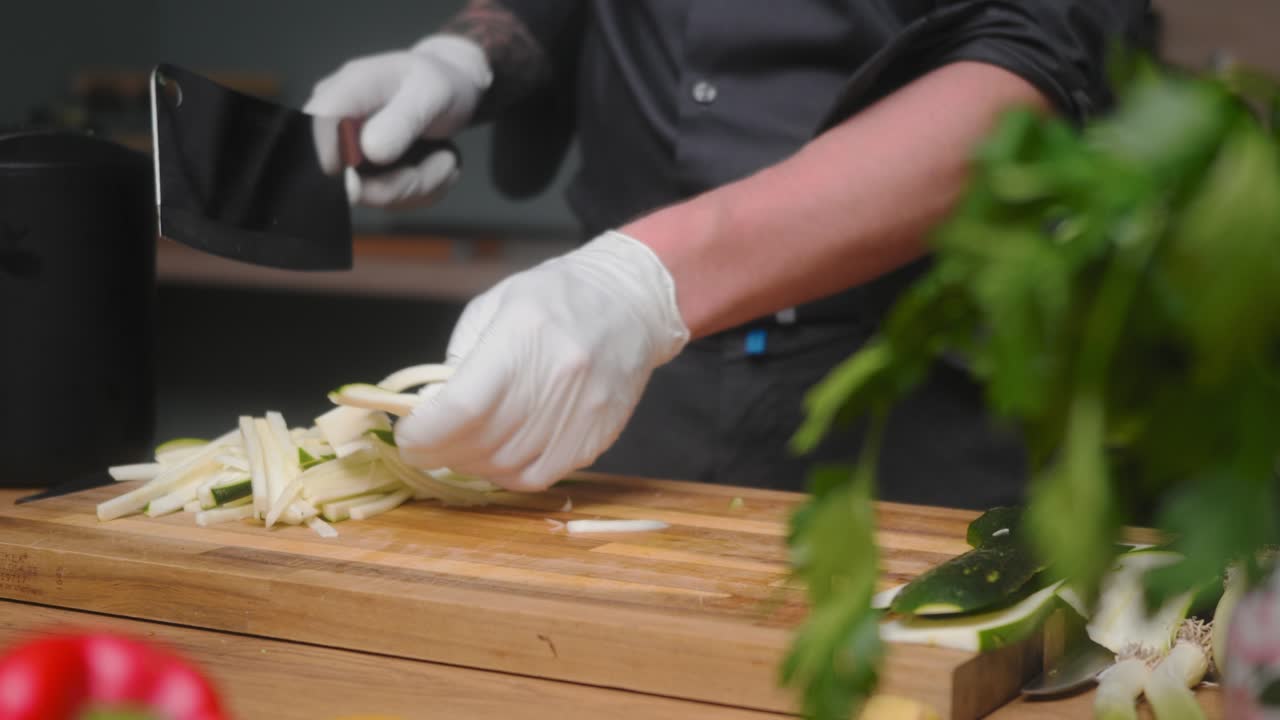 calabacín fresco cortado en una tabla de madera por un joven chef profesional con un elegante pantalones negro con tatuajes