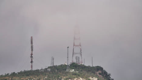 las torres de comunicación se revelan lentamente a través de las nubes en la cima de una montaña en un día gris tormentoso, mount stewart, townsville, australia