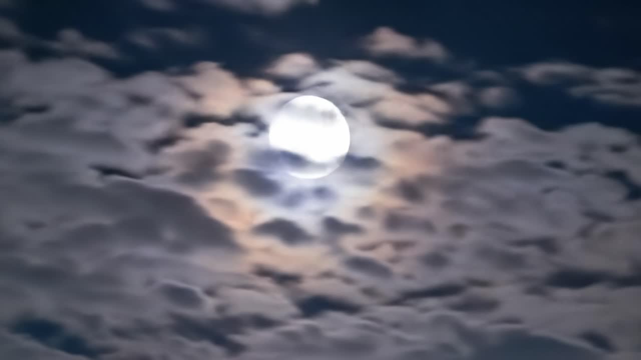 Bright moon shines through wispy clouds during a serene night. The peaceful atmosphere evokes calmness and wonder in the darkness of the sky.