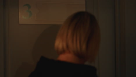 aesthetician in navy opens door with smile to welcome female client into bright treatment room featuring white walls and decorative flower vase, creating warm, inviting atmosphere for beauty service