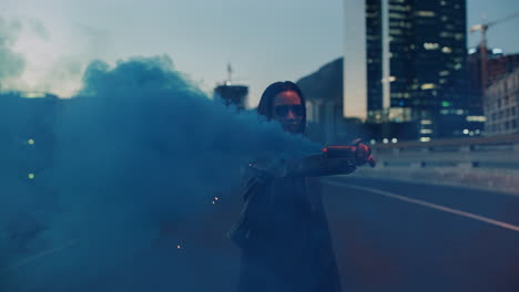 young woman holding blue smoke bomb in city at sunrise