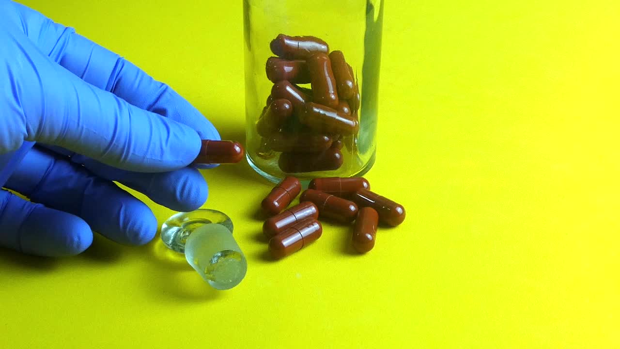 Pharmaceutical researcher taking a single brown capsule from a glass bottle on a yellow background