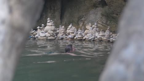 Woman swimming in a serene cave pool with stacked stones