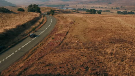 Disparo-De-Un-Dron-Después-De-Un-Auto-Antiguo-Black-Austin-Westminster-Conduciendo-A-Través-De-Las-Colinas-De-Sudáfrica-Durante-El-Invierno-Seco-4k