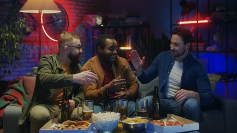 Razas-Mixtas-Amigos-Varones-Fanáticos-Del-Deporte-Viendo-Fútbol-Americano-En-La-Televisión,-Bebiendo-Cerveza-Con-Bocadillos,-Luego-Su-Amigo-Viene-Y-Se-Une-A-Ellos-Y-Animan-Juntos