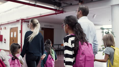 profesores masculinos y femeninos con un grupo de niños caminando en el pasillo de la escuela y yendo a clase