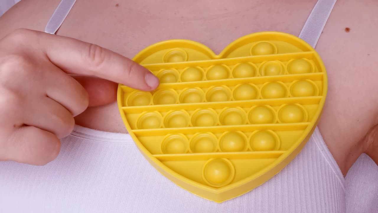 nuevo juguete para bebés. pop it juego de dedos. color gracioso. mano adulta apretando silicona redonda. cambio de forma. forma de corazón amarillo