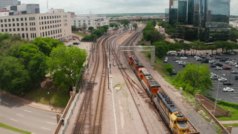 Drei-Leistungsstarke-Dieselmotoren-Führen-Einen-Güterzug-Um-Moderne-Wolkenkratzer-Mit-Glasfassade-Herum.-Luftdrohnenansicht-Des-Langsam-Fahrenden-Zuges,-Der-Am-Bahnhof-Ankommt.-Dallas,-Texas,-Uns