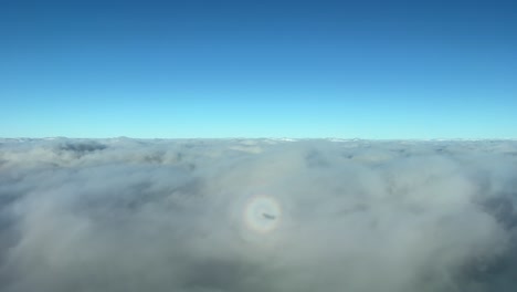 exclusive view from a jet cockpit overflying stratus clouds with the view of tha halo of the jet on the clouds