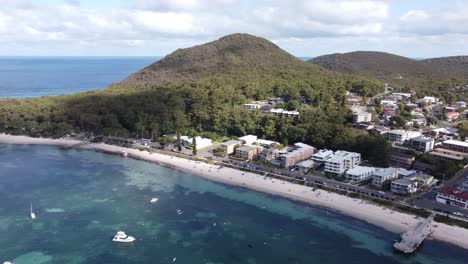 Aerial-view-of-a-coastal-town-with-sandy-beach,-boats-and-a-mountain-in-the-background