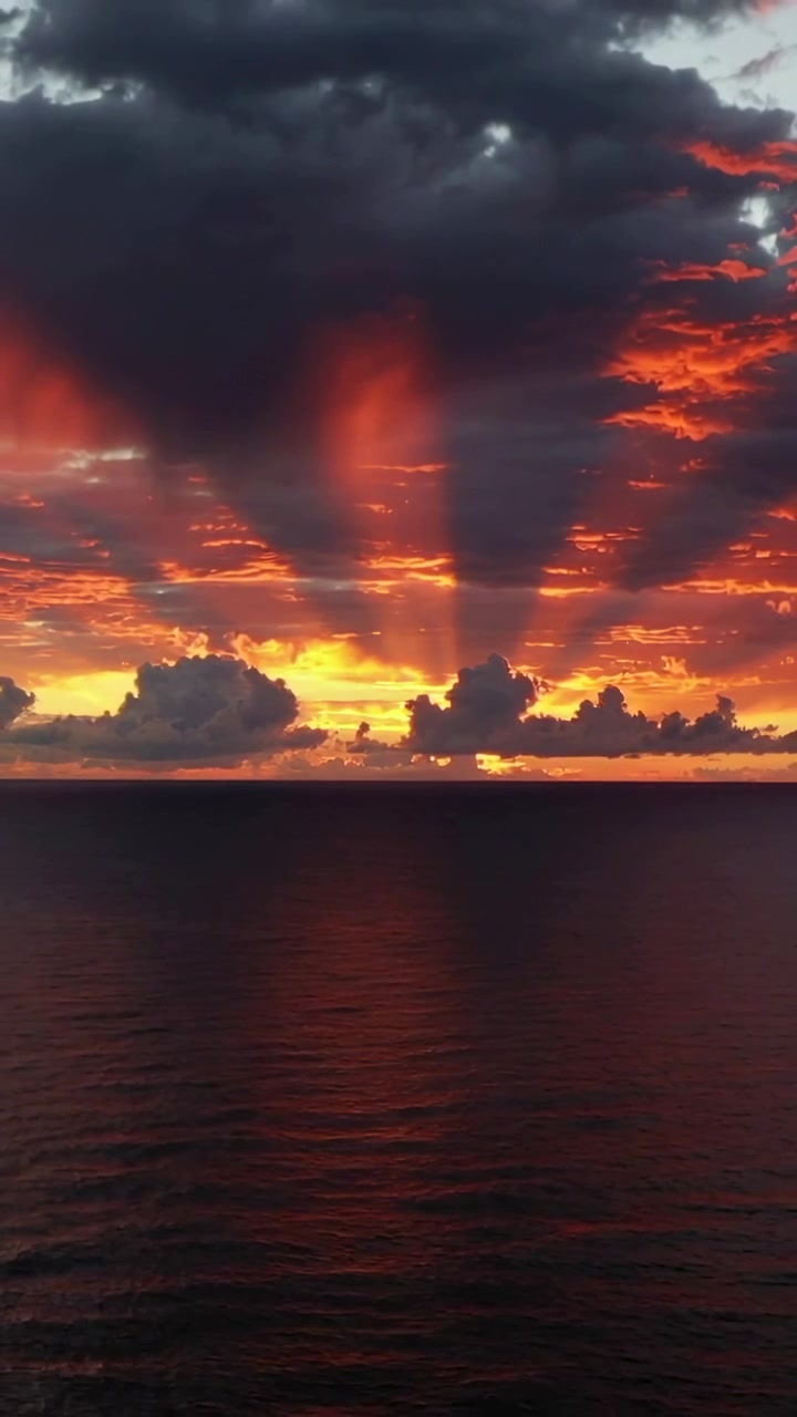 Vertical video: Casting crepuscular rays as sun slipping below horizon, sunset sky glowing over sea