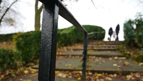 panning low shot through wrought iron hand rail as blurred people walk up steps in park