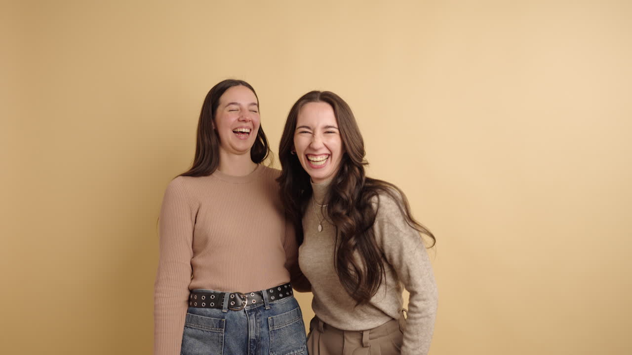 Two young women laughing together on a beige background