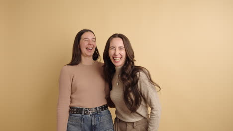 two young women laughing together on a beige background