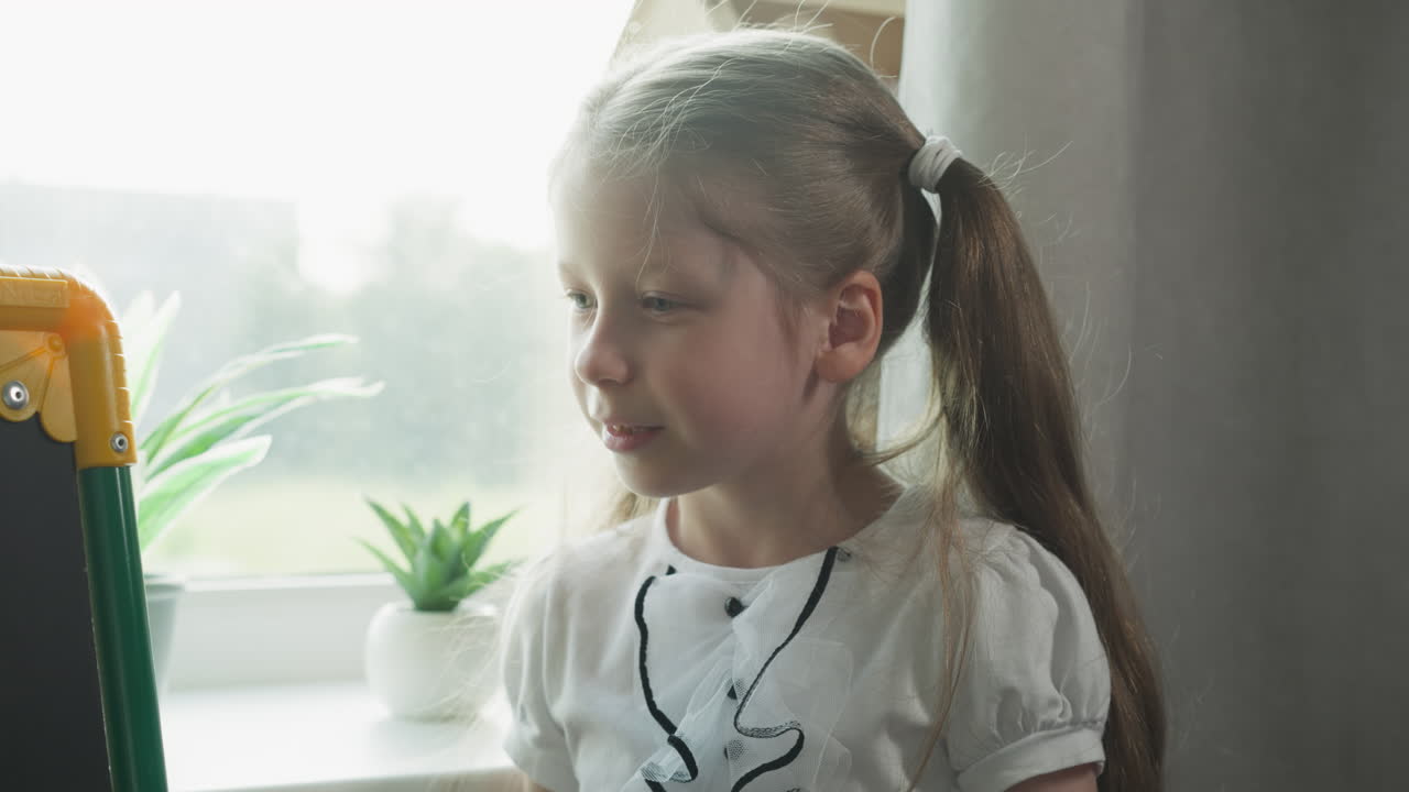 행복한 작은 소녀는 수업에서 작은 블랙보드에 머리를 돌린다