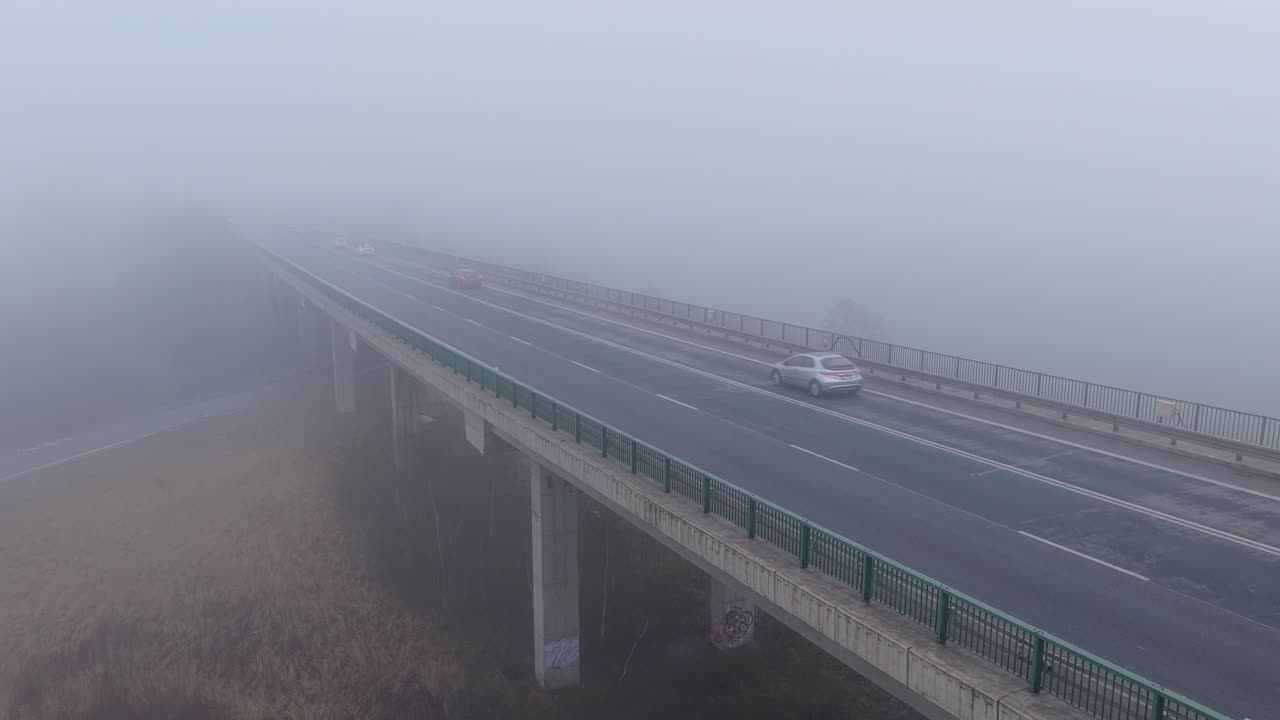 Cars slowly crossing a bridge on a wet road as thick fog creates a mysterious atmosphere after rain