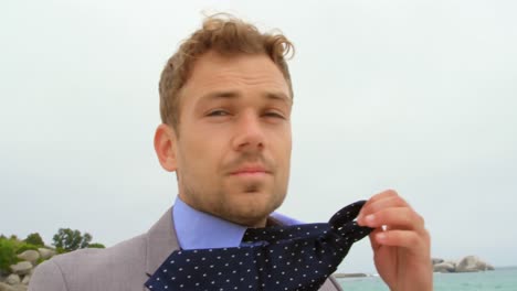 front view of caucasian businessman removing his tie on the beach 4k