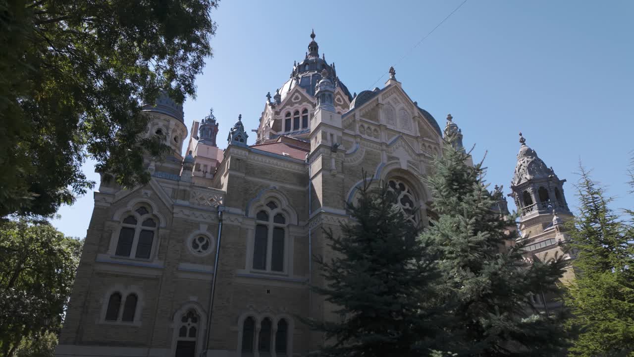 Hungary’s Szeged Synagogue wide exterior view with vibrant trees and clear sky, highlighting landmark design and heritage