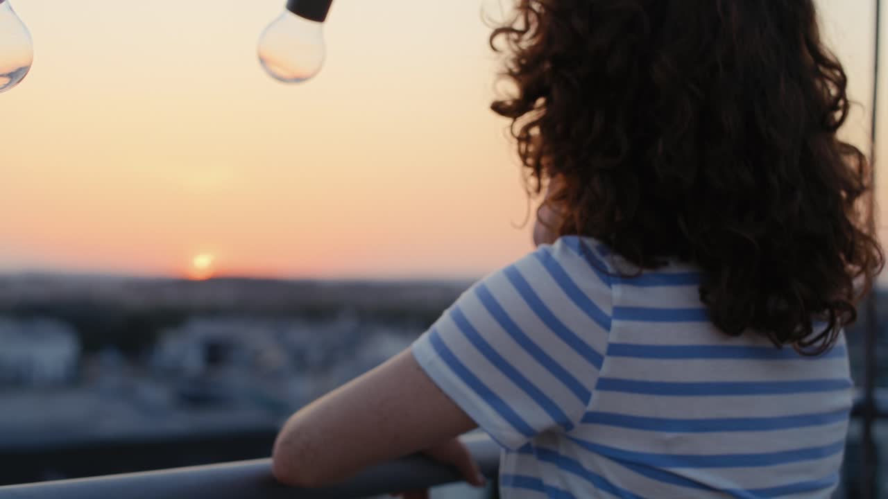 Donna dai capelli rossi in piedi che guarda il tramonto sul tetto in città.